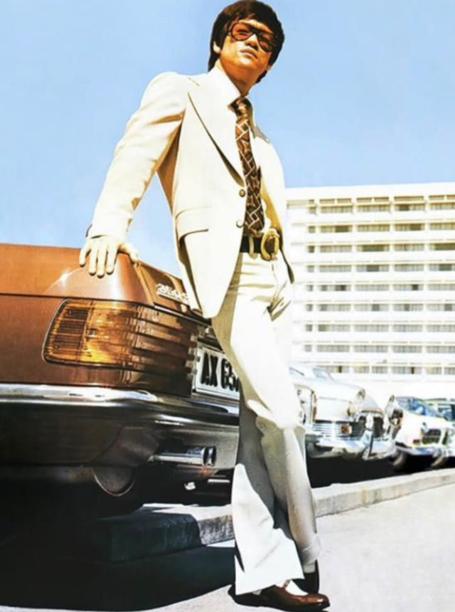Bruce Lee in a beige suit and amber aviator sunglasses, leaning on his Mercedes 350 SL in Hong Kong, early 1970s
