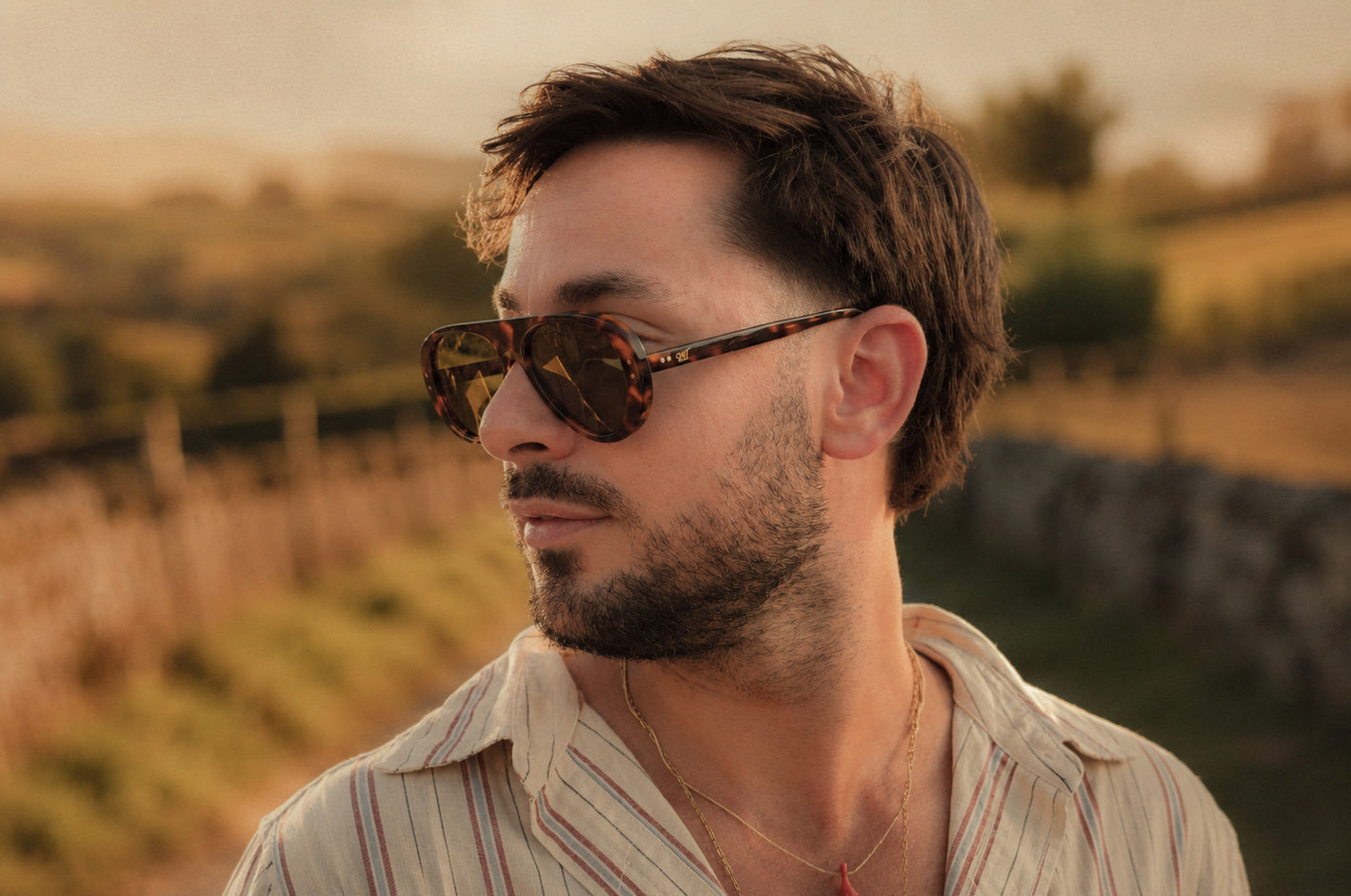 Man wearing SWT tortoiseshell aviator sunglasses outdoors at golden hour
