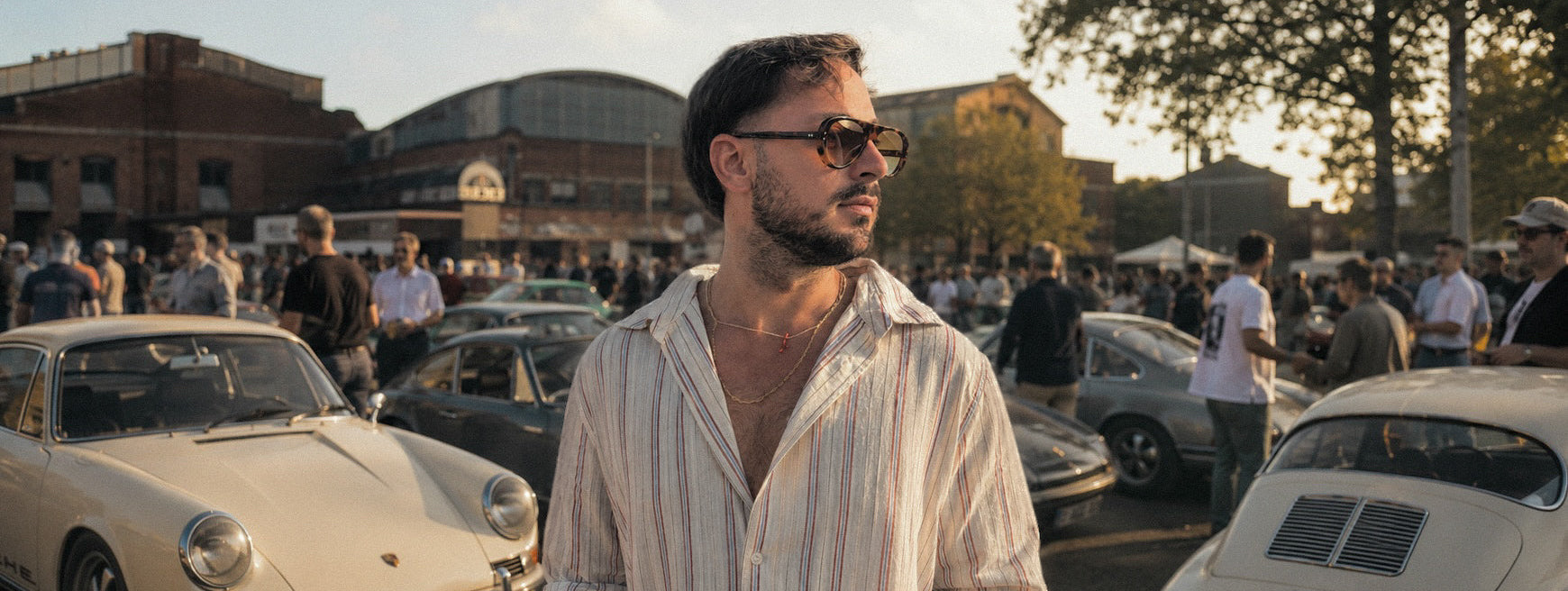 Man wearing SWT tortoiseshell aviator sunglasses, classic cars behind
